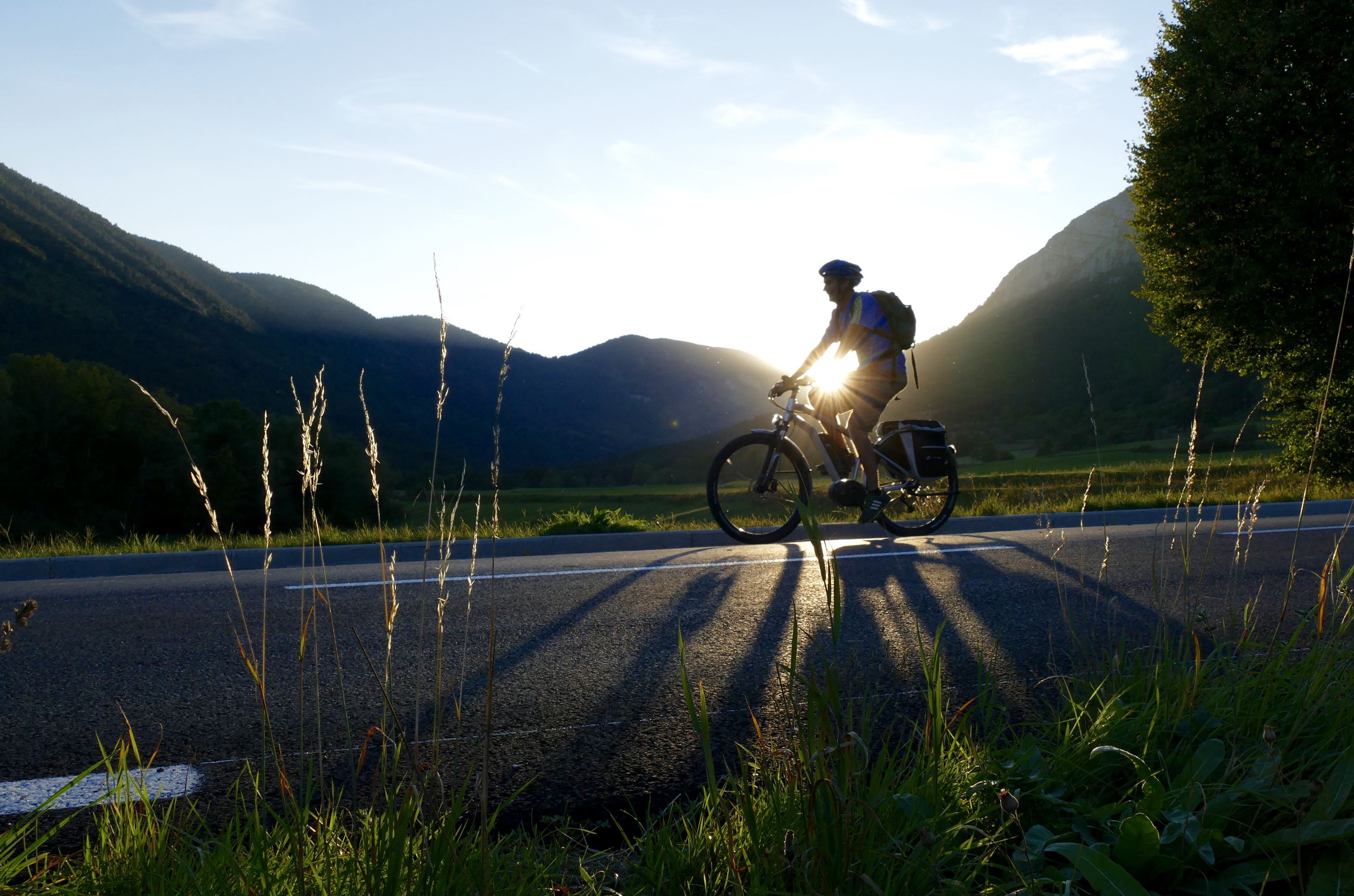 Image of a silhouette of a bicyclist  riding down a road against a sunset and a mountain 